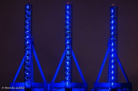 Drei blau angestrahlte Kräne im Hamburger Hafen